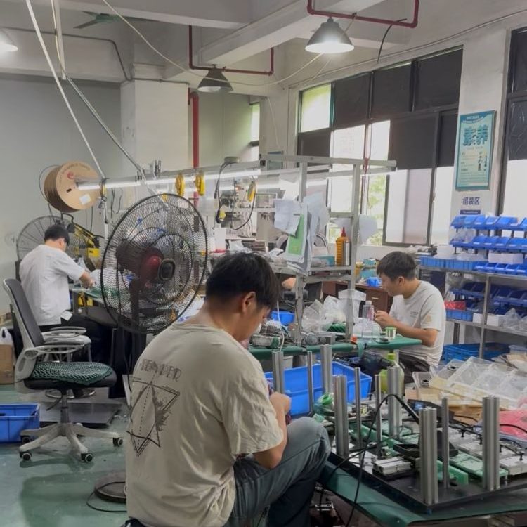 Workers assemble custom test jigs and fixtures at assembly workstation inside manufacturing factory